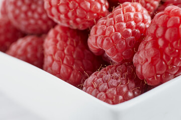 Close-up photo of raspberries in a white bowl.