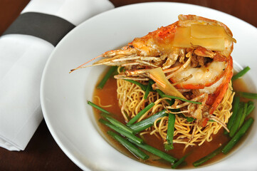 Yee Mee Fried Noodle with Big Prawn on top and some spring onion on top, served in a white plate.