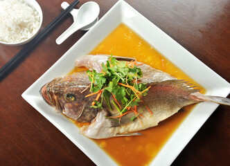 Steamed whole Grouper Fish in soy sauce of Chinese cooking style and garnish with shredded ginger and parsley,
served on wooden table.
