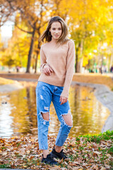 Young girl in a woolen sweater and torn jeans posing in an autumn park