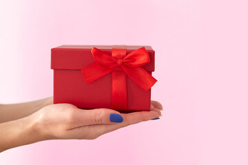 Woman's hands holding red gift box with bow on pink background. Side view.
