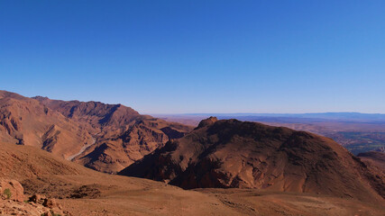 Beautiful panoramic view of the southern foothills of the Atlas Mountains near Tinghir, Morocco with the entrance to famous Todgha Gorges and red colored rocks on a cold winter day with blue sky.