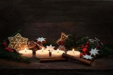 Four small candles lit for Advent and Christmas decoration like gingerbread cookies, branches and...