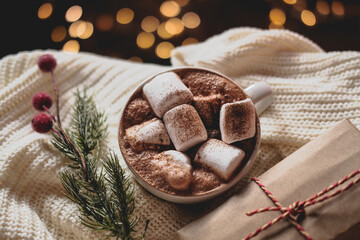 Christmas hot chocolate with added marshmallows and cinnamon, lights bokeh, a sprig of Holly ,pine cones, gift
