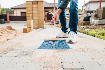A man with a brush sweeps the paving slabs on the path near the house - general cleaning of the...