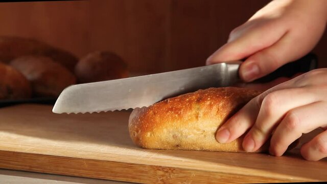 Female hands slicing with a knife crusty bread with olives on wooden table in the kitchen on a sunny day