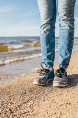 Slender female legs in jeans and sneakers - a walk along the North Sea in the non-resort season - an empty beach
