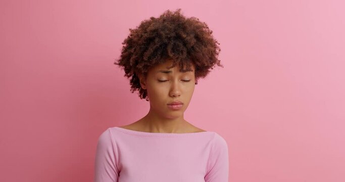 Slow motion beautiful young woman with Afro hair grimaces as if looking at something disgusting or ugly frowns face with aversion dislikes something unpleasant poses against pink background.