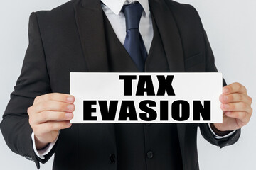 A businessman holds a sign in his hands which says TAX EVASION