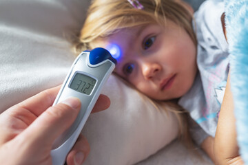 Parent takes temperature for her child with infrared thermometer at home, low-grade fever