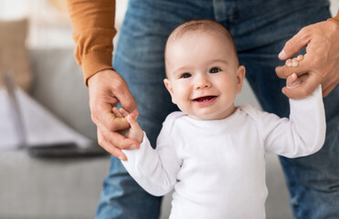 Smiling Baby Toddler Making First Steps Holding Father's Hands Indoors