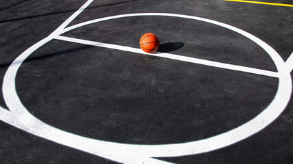orange striped basketball ball stands in circle on the marking playing field with asphalt tarmac,...