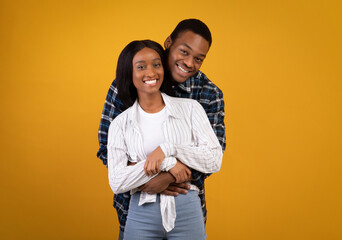 Cheerful young african american male and female in casual, hugging and looking at camera