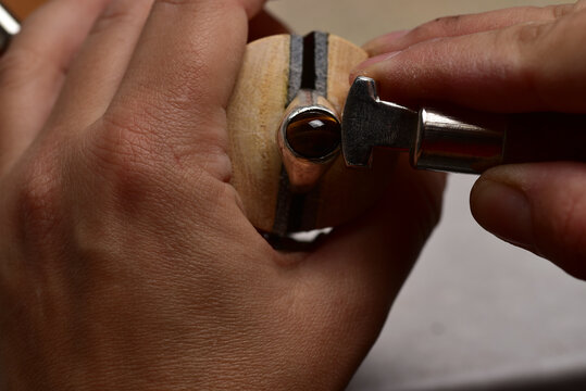 Jeweler making bezel setting for the silver ring with a cabochon tiger eye stone