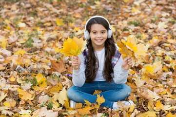 Fototapeta na wymiar In love with nature. autumn kid fashion. inspiration. happy childhood. back to school. girl among maple leaves in park. fall beauty in park. enjoy music in earphones. education online and e-learning