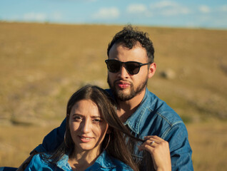 A romantic and lovely latin couple sitting together a beautiful sunny day with a dry grass field and a sunset in the background