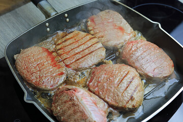 Frying rump steak medallions in a frying pan.