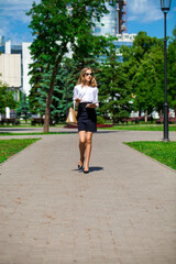 Young business blonde woman walks in a summer park