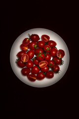 Cherry tomatoes on a white plate on a black background, close up top view