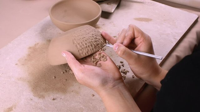 A potter is decorating a clay bowl