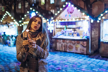 Christmas, New Year. Woman burning sparkler on city street fair in Lviv. Girl having fun outdoors on holidays