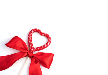 Bow with a heart-shaped Lollipop on a light background. Top view with space to copy. Concept of holiday backgrounds.