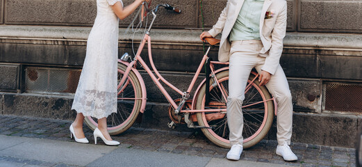 Wedding couple together posing on a pink bicycle at street. Wedding agency concept.