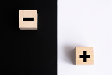 Symbols of black color plus and minus on wooden cubes on a white and black background. Abstraction