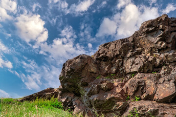 Rock on top of the mountain against the background of a blue summer sky and white cumulus clouds.