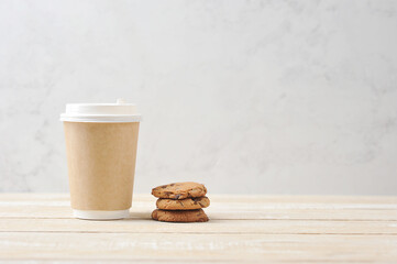 Paper glass with a hot drink on a light wooden background.  Oatmeal cookies with chocolate chips next to a glass.  The concept of a quick and tasty snack.