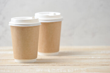 Coffee to go concept. Two paper cups with lids. Free space for text placement. Light wooden background. Close-up.
