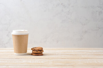 Paper glass with a hot drink on a light wooden background.  Oatmeal cookies with chocolate chips next to a glass.  The concept of a quick and tasty snack.