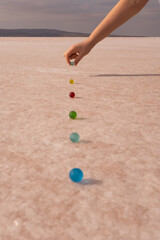 colourful marbles made of glass arranged on a flat surface. woman hand adds a ball. round objects on the salt lake.