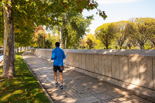 man jogging in the city in autumn. he wears a blue coat and shorts. autumn colors in the city.