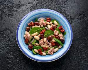Tuna, white bean salad with olive, red onion, spinach and dried tomato. Healthy food.