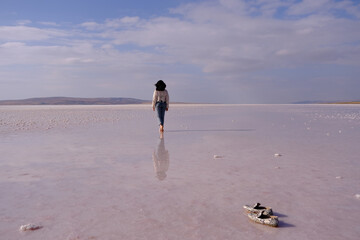 woman walking on salt lake with blue sky background. her reflection on shallow water. the concept of peace, quiet, loneliness and rest. she left behind her shoes and wearing a lace patterned shirt.