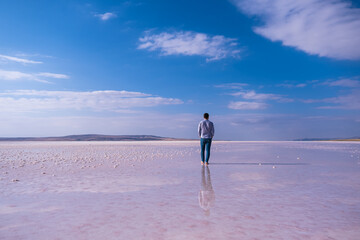 man walking on the salt lake with the blue sky background. his reflection on shallow water. the concept of peace, quiet, loneliness and rest.