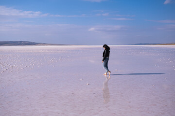 woman with leather jacket walking on the salt lake with the blue sky background. woman's reflection on shallow water. the concept of peace, quiet, loneliness and rest.