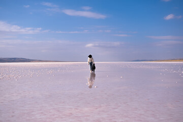 woman walking on the salt lake with her jacket in hand. woman's reflection on shallow water. the concept of peace, quiet, loneliness and rest. the woman is wearing a lace patterned shirt.