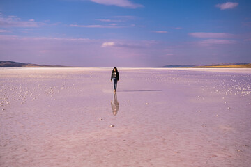 woman with leather jacket walking on the salt lake with the blue sky background. woman's reflection on shallow water. the concept of peace, quiet, loneliness and rest.