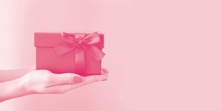 Woman's hands holding red gift box with bow on pink background. Side view, holiday present concept with copy space, banner.