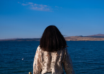 woman watching the sea with the blue sky background. the concept of peace, quiet, loneliness and rest. the woman is wearing a lace patterned shirt.