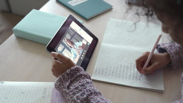 African american school kid child girl holding digital tablet talking to remote teacher tutor on social distance video conference call study online virtual class learning at home, over shoulder view.