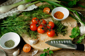 Still life with cherry tomatoes, onions, dill, chicken, spices, garlic, paprika and salt on a wooden board