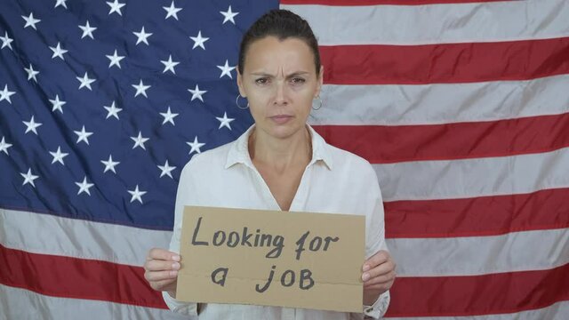 Unemployed woman with cardboard. An upset needy woman looking for a job with a cardboard on the background of American flag.