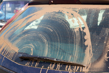 dirty car suv covered with a dry layer of dust from soil smeared with a windshield wiper closeup...