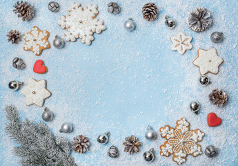 Gingerbread cookies, fir cones and Christmas balls on a blue snowy background in the form of a frame. Christmas background, texture, concept, top view.