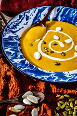 blue spatterware soup plate filled with pumpkin bisque garnished with swirl of cream and sprinkled with dried pumpkin seeds.