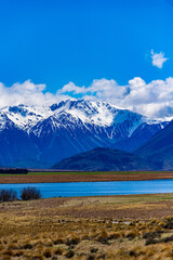Snow covered mountains and green valleys with a lake in New Zealand