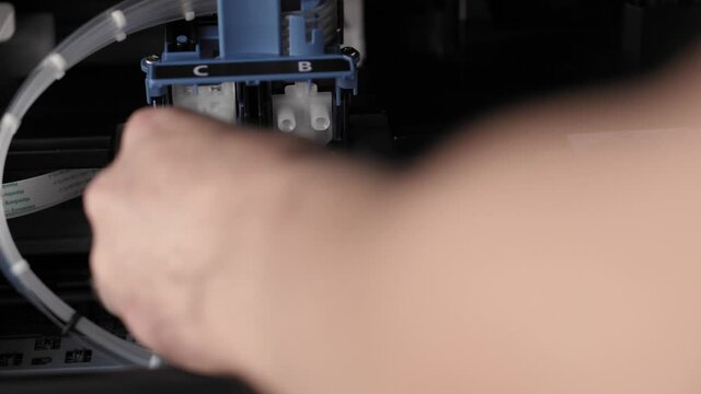 Video instruction, technology, press, media, office, stationery concept - close-up of male hands preparing new inkjet printer for launch. step 4: instaling color and black cartridge in locking cover